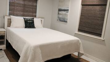 A neatly made bed with a white bedspread, a pillow with text, and a painting on the wall.