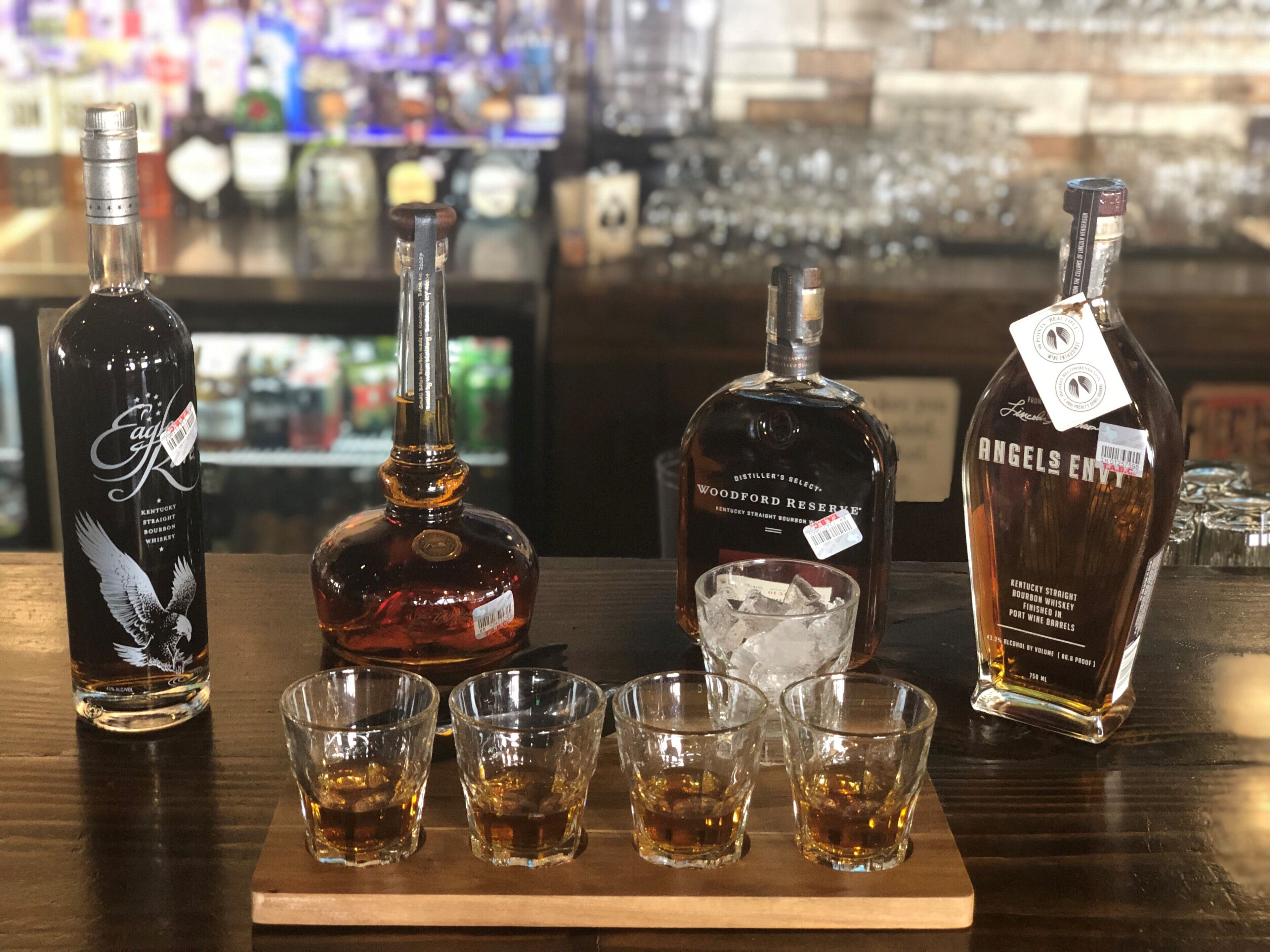 A bar setting with three bottles of whiskey and four shot glasses filled with whiskey.