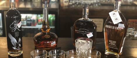 A bar setting with three bottles of whiskey and four shot glasses filled with whiskey.