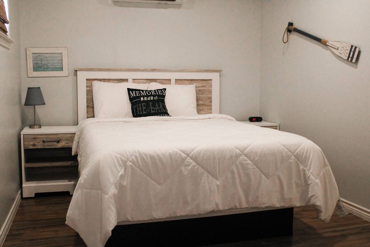 A neatly made bed with a quilted white comforter, a wooden headboard, and a pillow with a printed message.