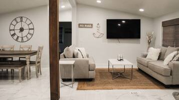 A modern living room with a dining area, a large wall clock, a flat-screen TV, and a 'NO WAKE' sign.