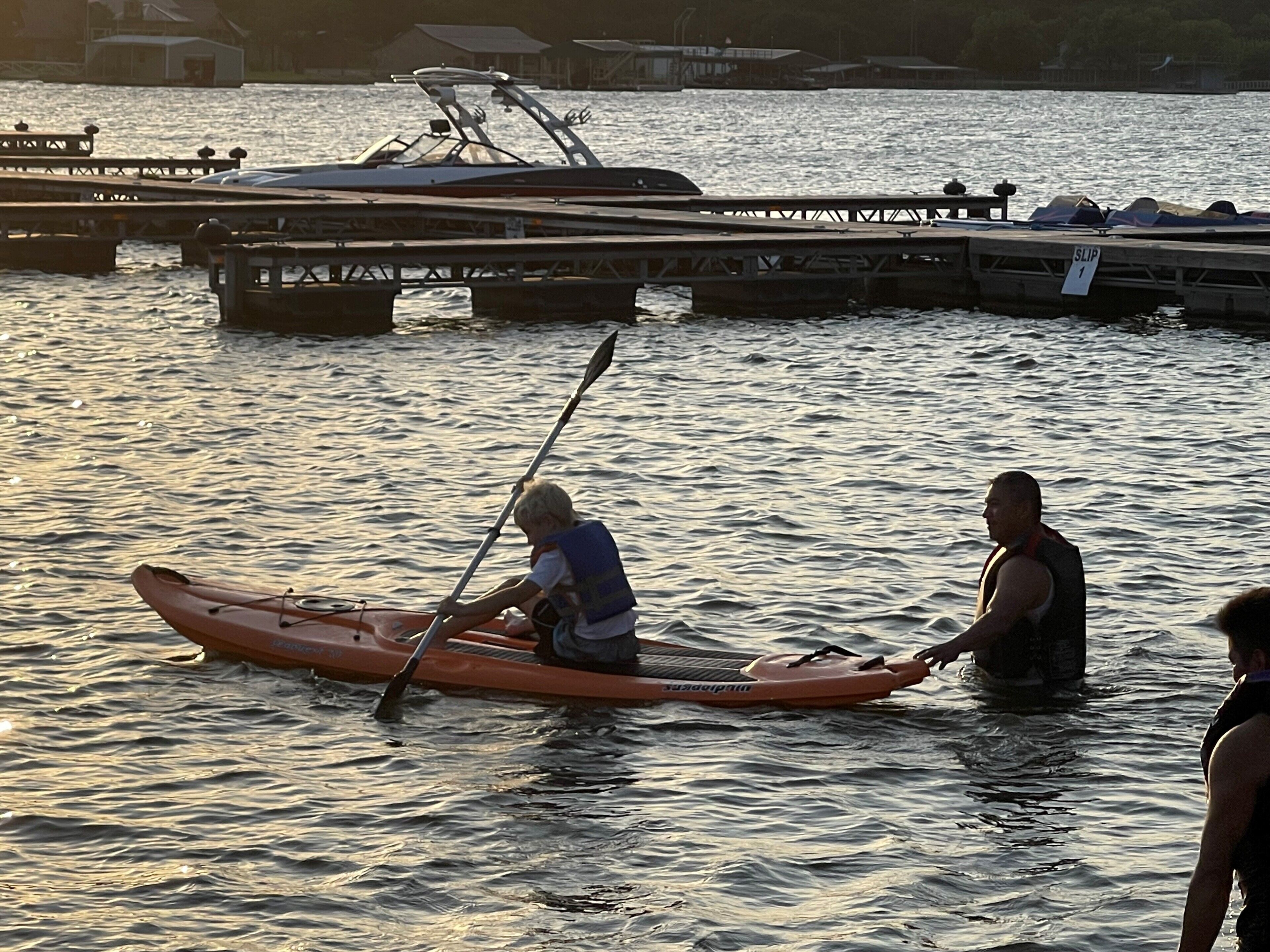 A person in a kayak on a body of water with a dock in the background.