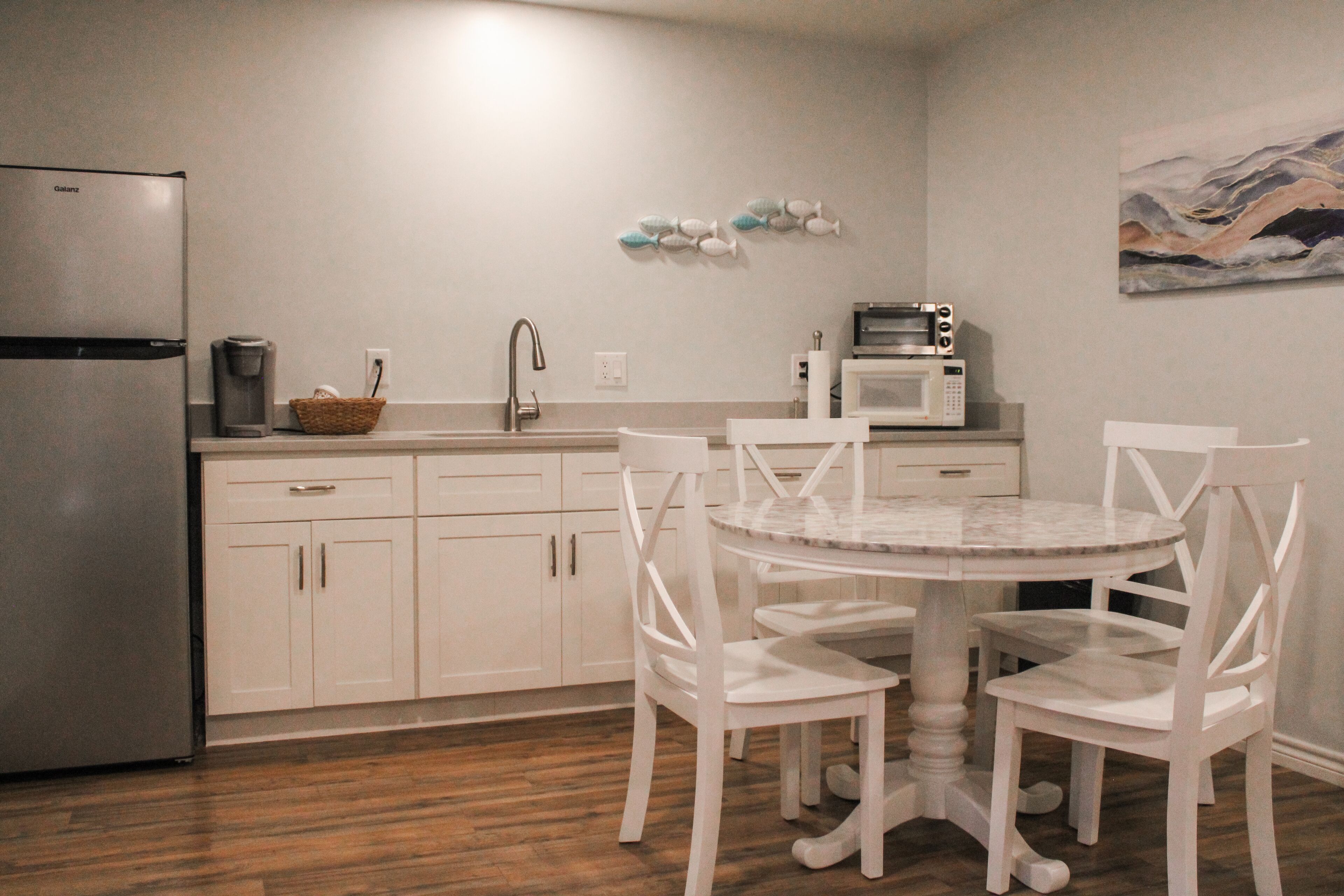 Una cocina moderna con armarios blancos, un refrigerador de acero inoxidable, un microondas y una mesa de comedor con sillas blancas.