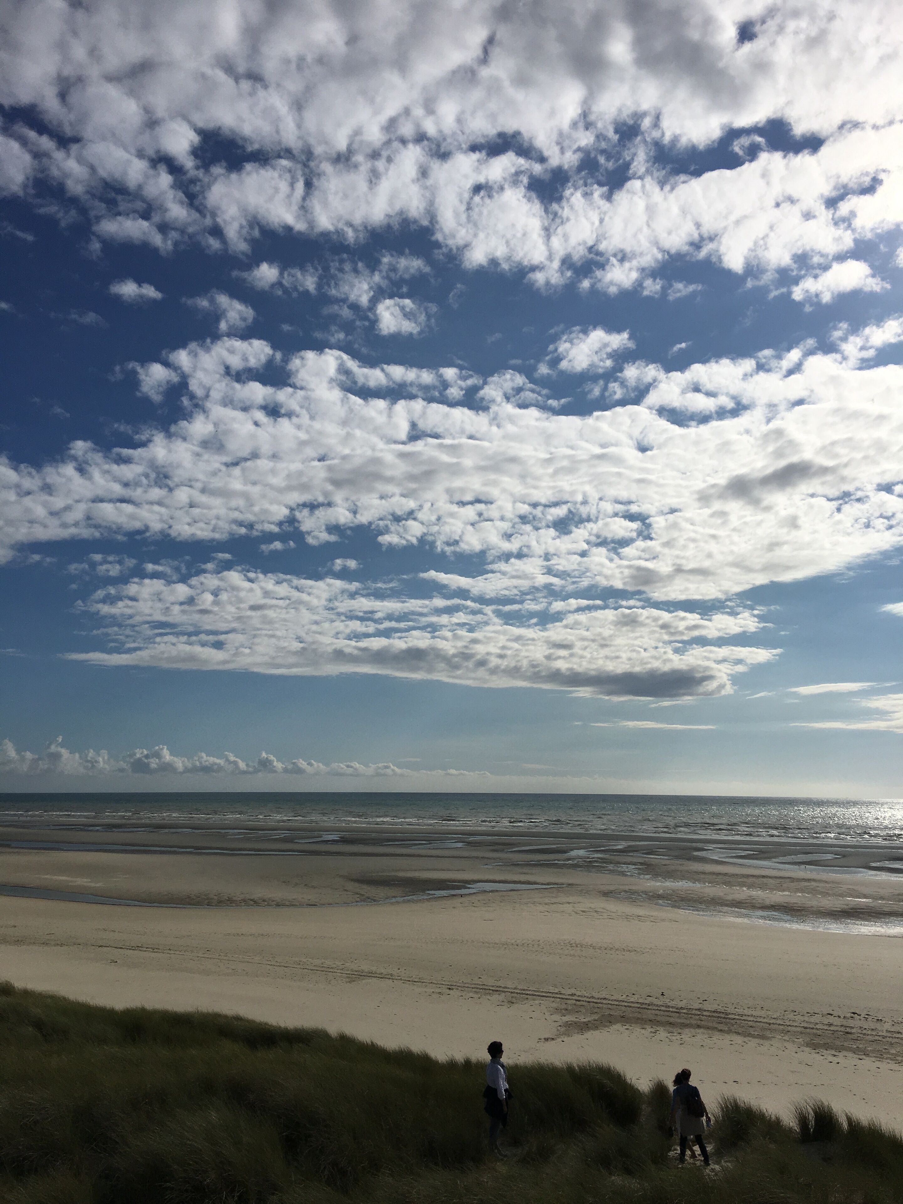Uma praia com extensa faixa de areia e dunas gramadas ao primeiro plano.