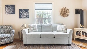 A living room with a grey sofa, patterned armchair, and a fireplace. - Serendipity- A Historical 1882 Beach Cottage (Pacific County)