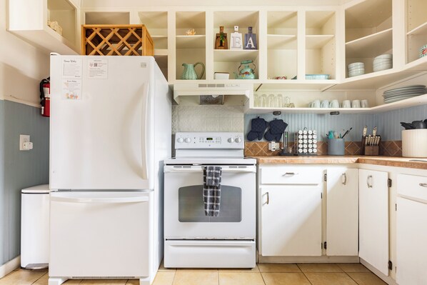 Eine Küche mit weißem Kühlschrank, Herd und Backofen, Holzschränken und einer gefliesten Spritzschutzwand.