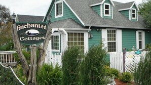 A green cottage with a white picket fence and a sign reading "Enchanted Cottages." - Serendipity- A Historical 1882 Beach Cottage (Pacific County)