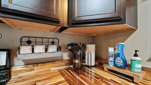 Eine Küche mit Holzboden, einem Metallregal mit Küchenutensilien und einer Ablage für Reinigungsmittel.