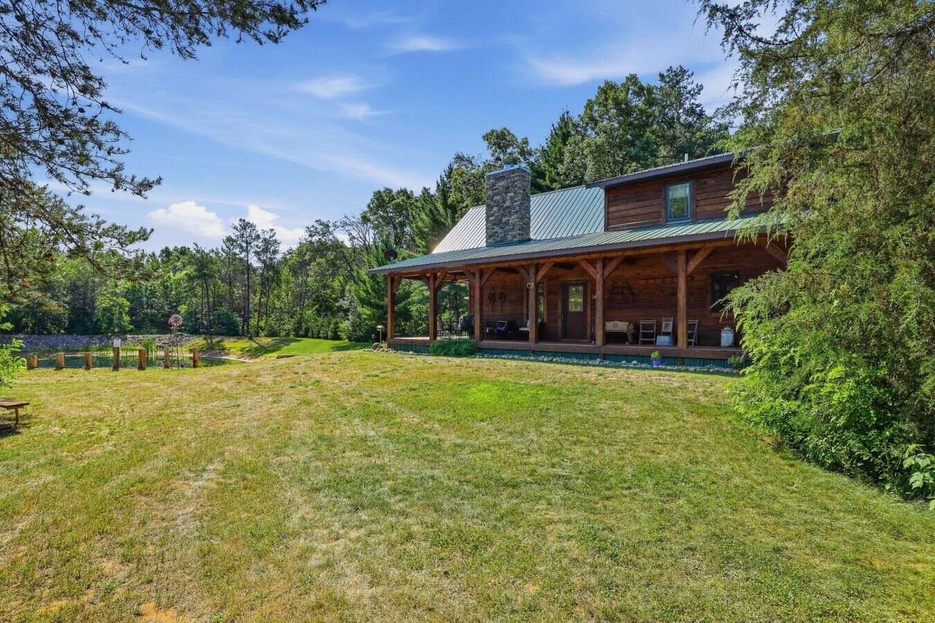 A wooden cabin with a porch, surrounded by a grassy yard and trees.