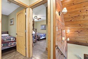 A room with a wooden door, a bed with a patterned blanket, a ceiling fan, and a framed picture on the wall. - Little Cabin in the Big Woods - Cabin #2 (Necedah)