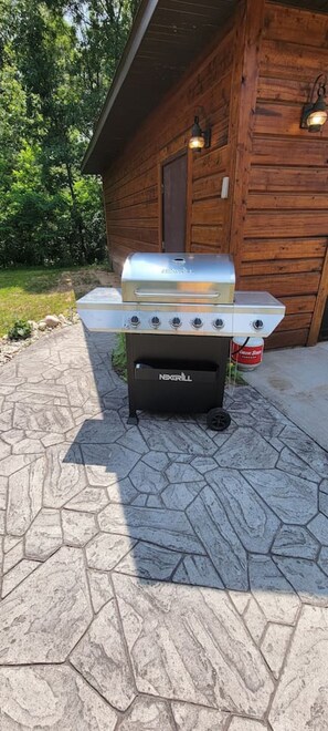 A portable grill with a built-in side burner and a separate grill box, placed on a stone patio in front of a wooden cabin. - Little Cabin in the Big Woods - Cabin #2 (Necedah)