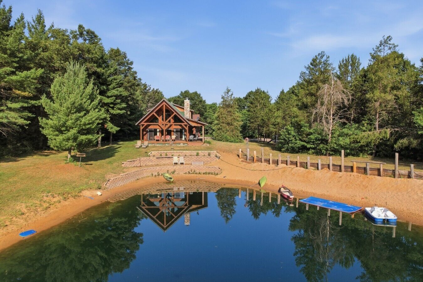 A lodge with a reflection in a pond, surrounded by trees.