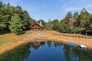 A lodge with a reflection in a pond, surrounded by trees.