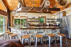 A rustic kitchen with a stone island, bar stools, and a large refrigerator.