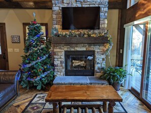 A cozy living room with a stone fireplace, a Christmas tree, and a flat-screen TV mounted above it. - Little Cabin in the Big Woods - Cabin #2 (Necedah)
