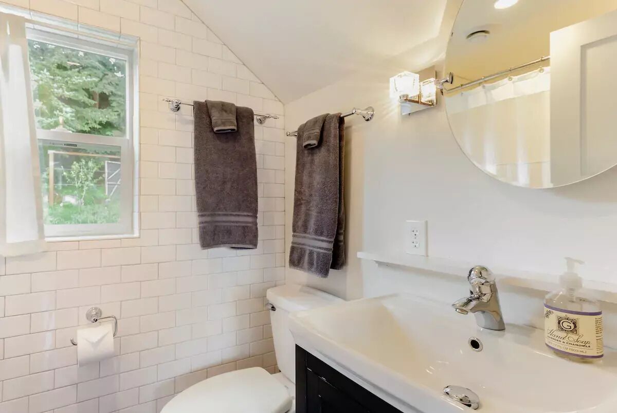 A bathroom with white tiled walls, a white sink with a chrome faucet, and two towels hanging on hooks.