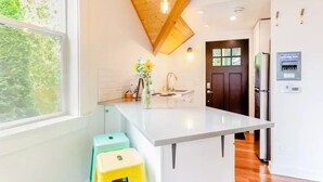 Una cocina moderna con una isla central, una ventana con vistas a la vegetación y una puerta que da a otra habitación.