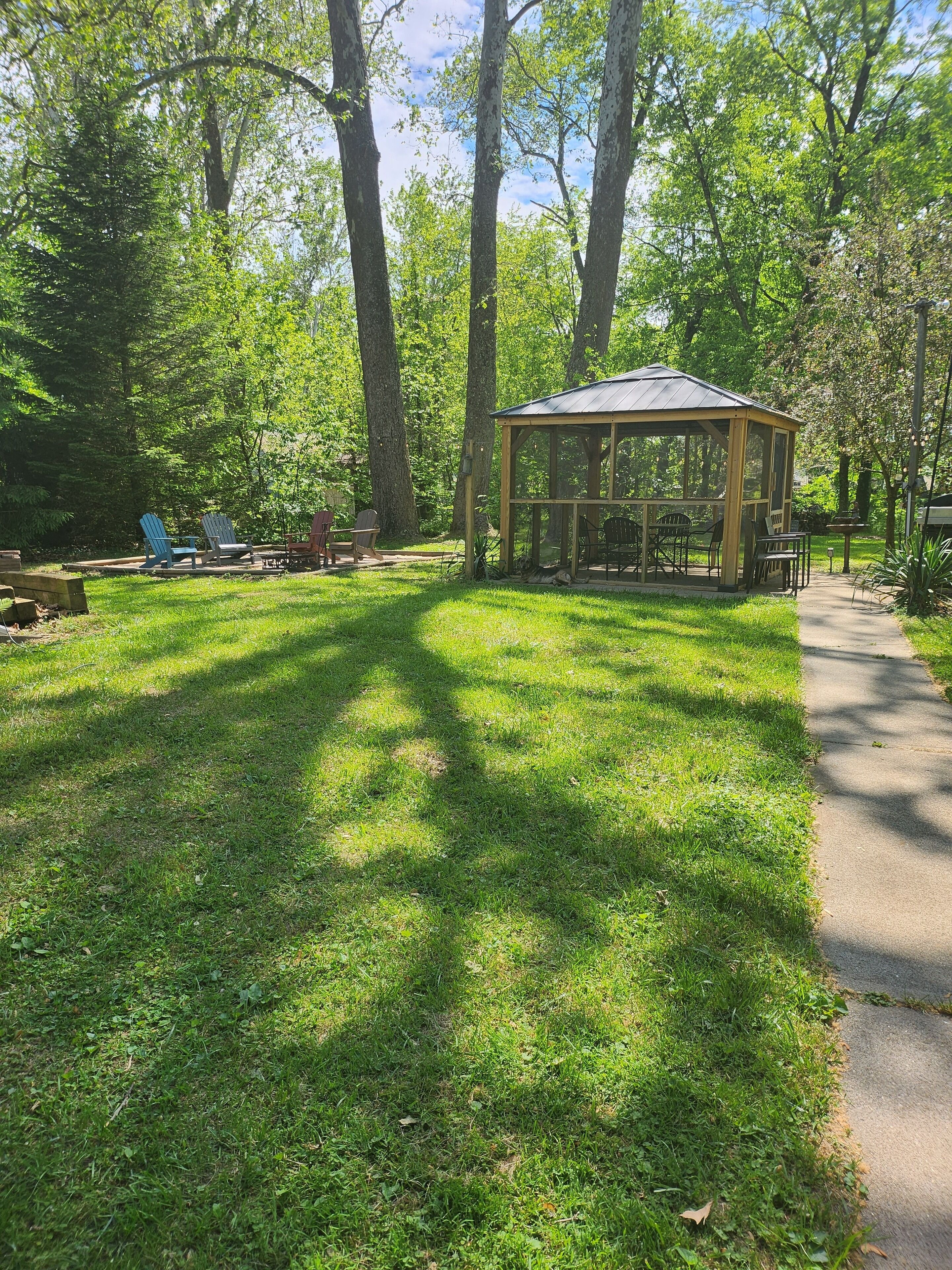A gazebo with a roof and open sides, surrounded by a grassy area with trees.