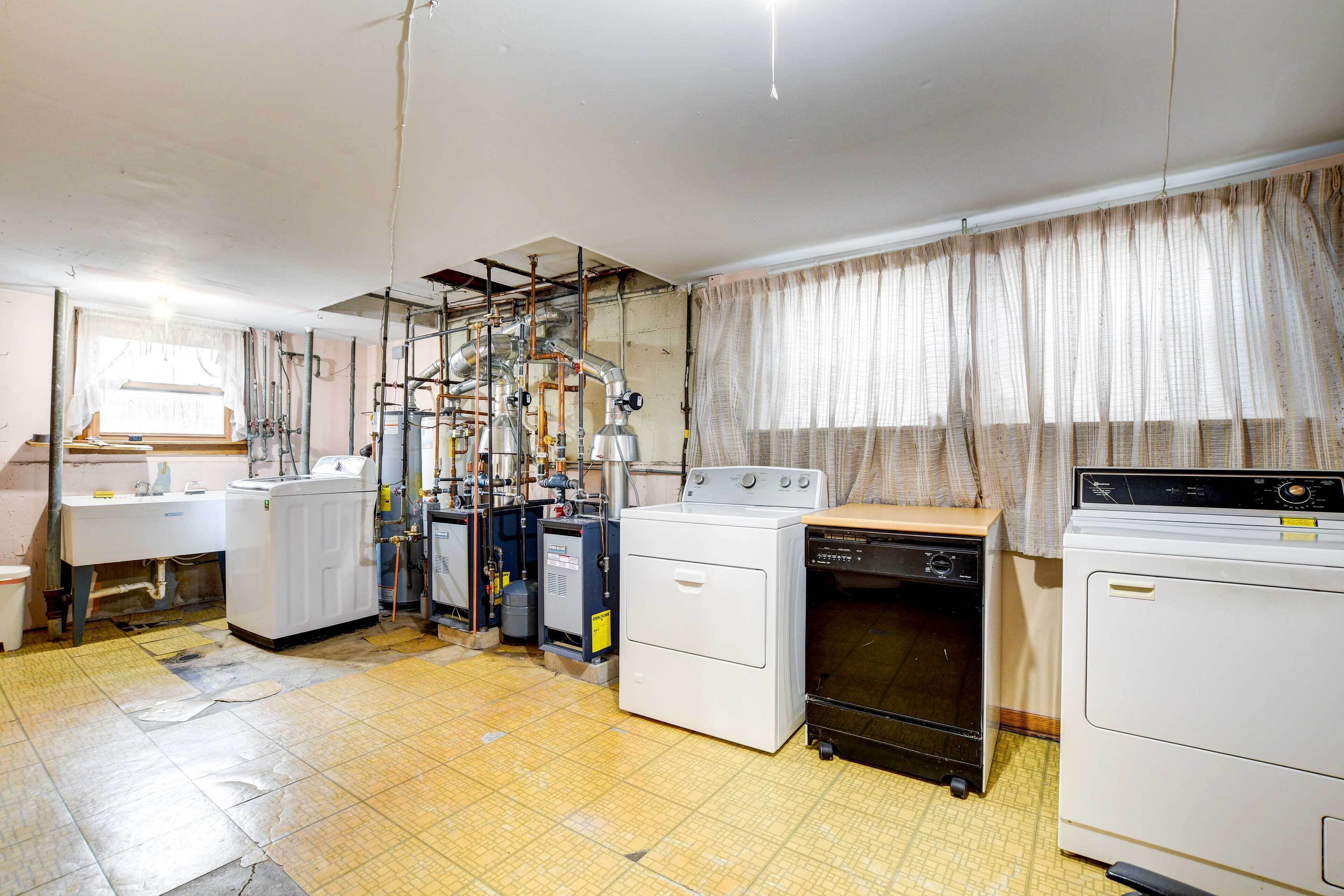 A laundry room with multiple washing machines, a sink, and exposed pipes on the ceiling.