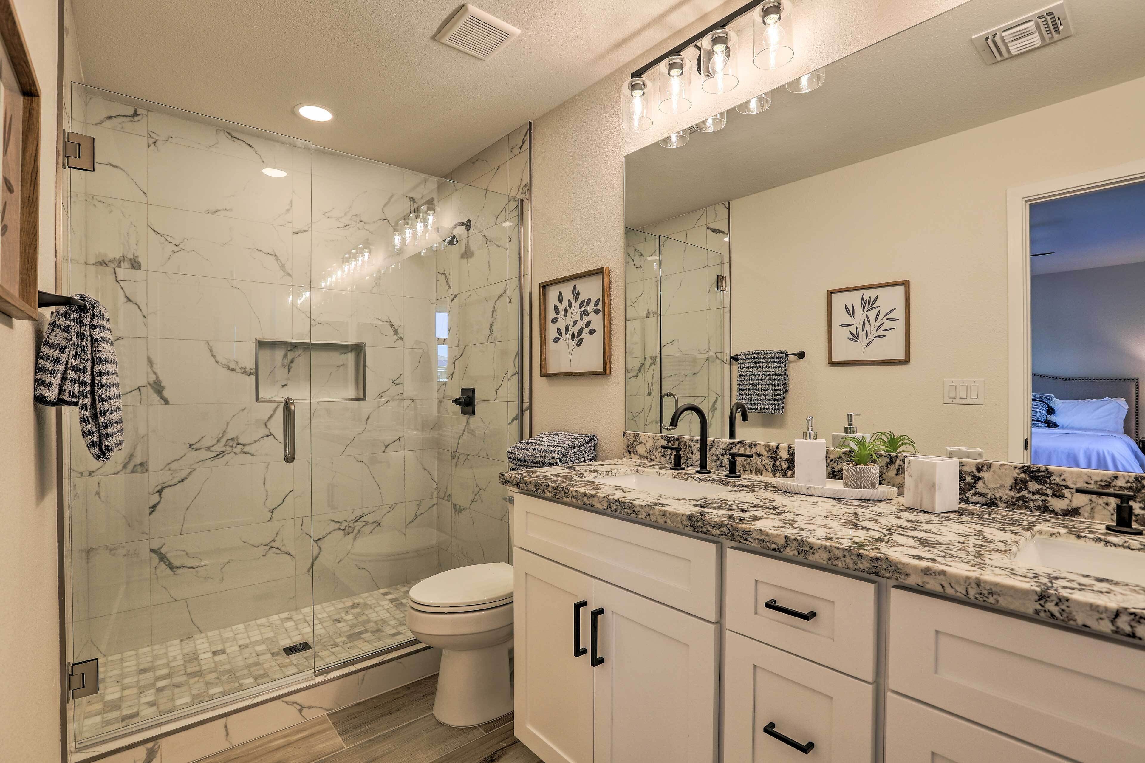 A modern bathroom with a glass shower enclosure, a toilet, and a vanity with a large mirror.