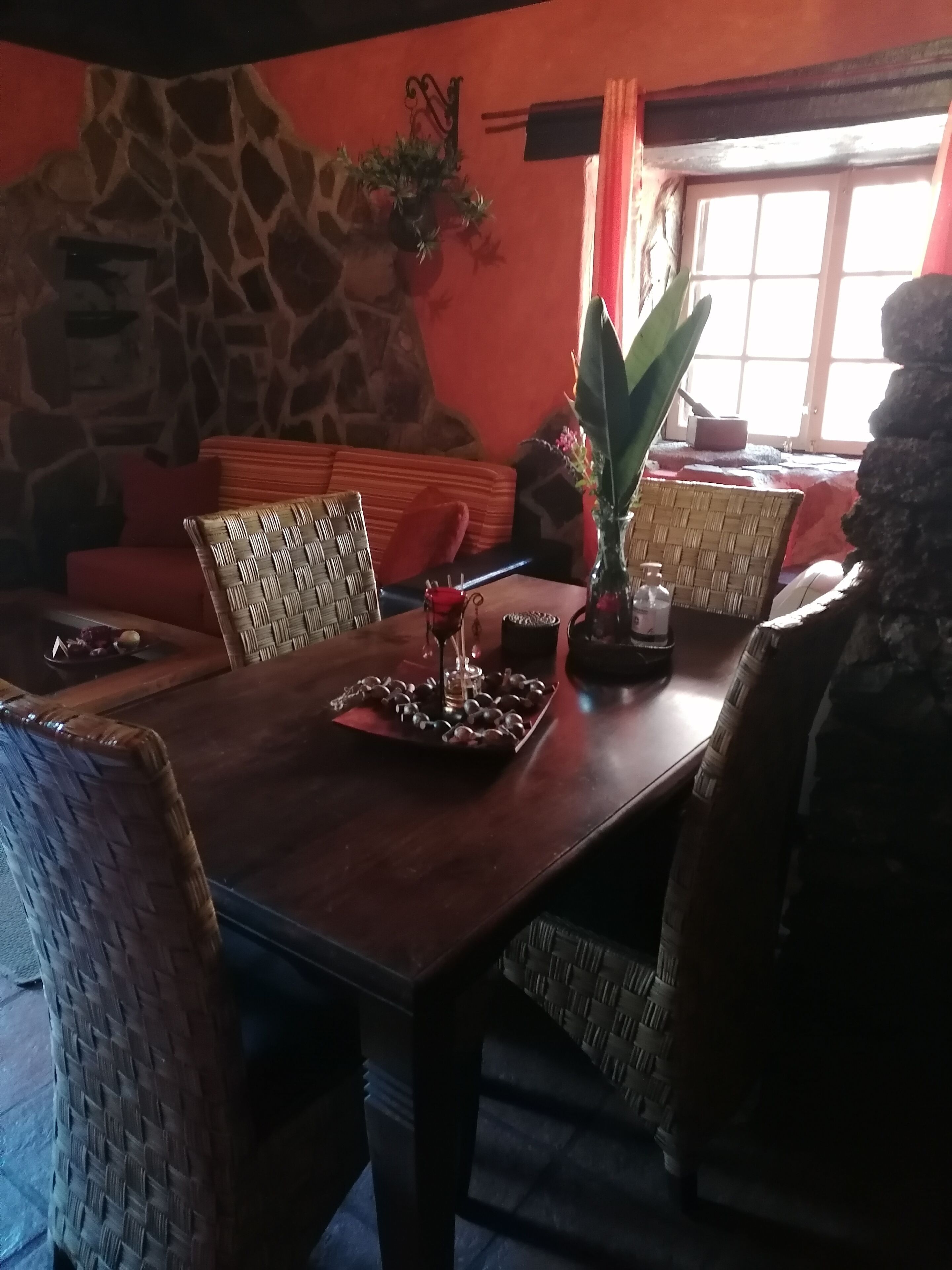 A dining area with a stone wall, wicker furniture, and a table set with a glass, a red rose, and a tray of chocolates.