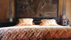 Ein Bett mit einer gesteppten Decke und zwei Kissen, dahinter eine Steinwand und eine Holzbalkendecke.