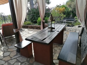 Eine Terrasse im Freien mit einem Holztisch und Bänken, umgeben von Steinplatten und Pflanzen.