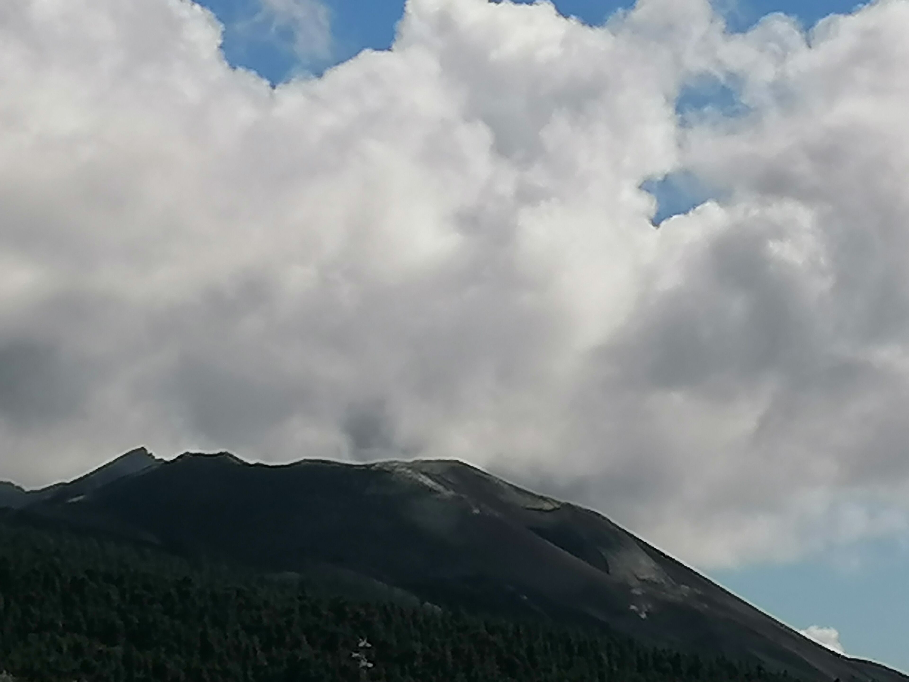 A mountain with a forested slope and a partly cloudy sky.