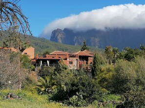 Eine rustikale Villa mit Naturstein-Fassade, Terrakotta-Dach und Blick auf einen Berg und Wolken.