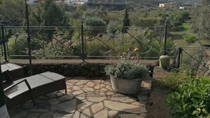 Eine Terrasse mit Steinbelag, Gartenmöbeln und Blick auf eine gebirgige Landschaft.