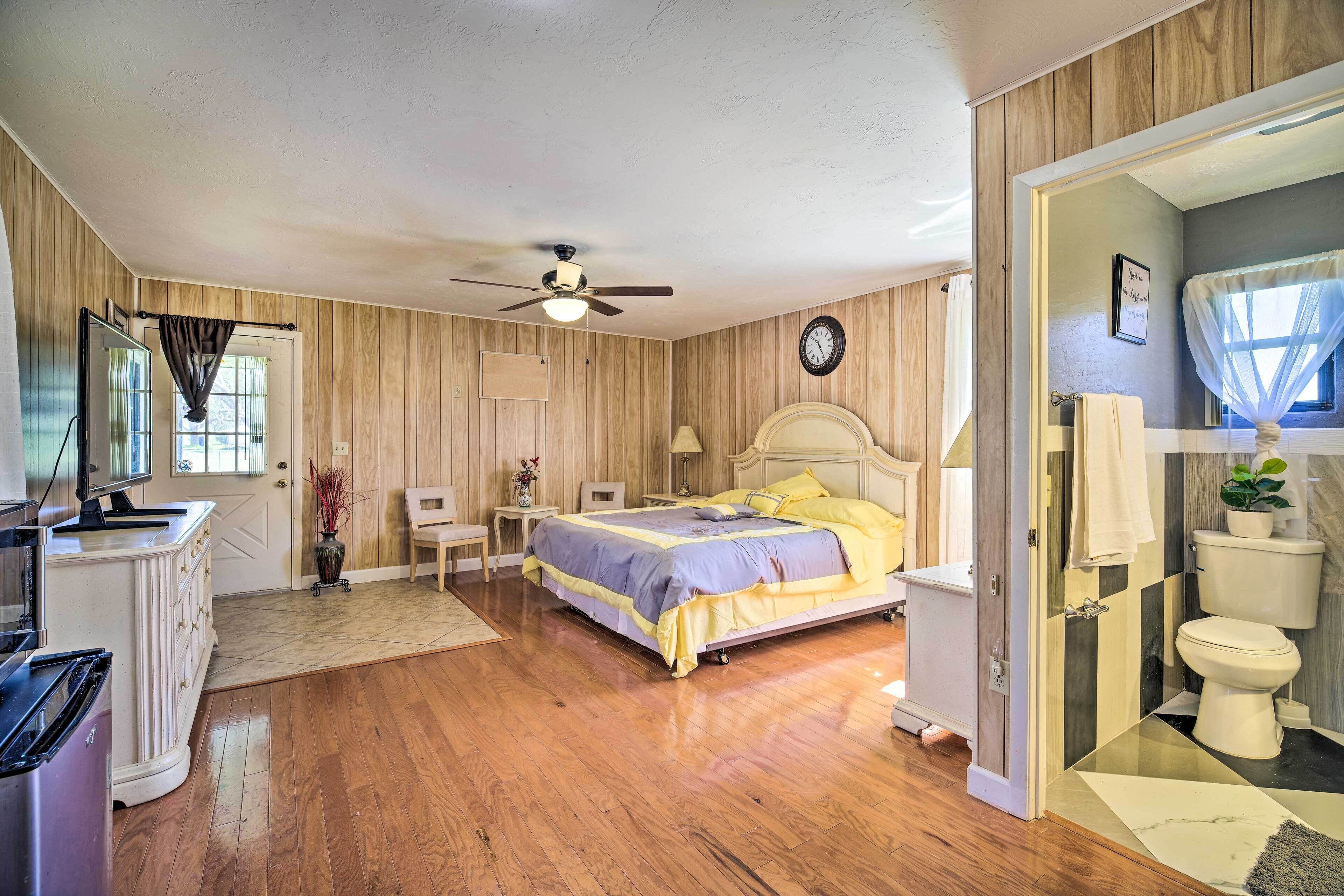 A bedroom with a bed, a ceiling fan, a dresser, a television, and a bathroom with a toilet and sink.
