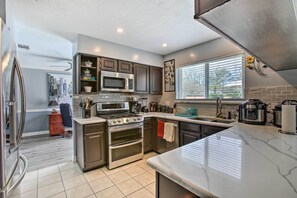 A modern kitchen with stainless steel appliances, a marble countertop, and a window with blinds. - Houston Home with Private Outdoor Pool! (Houston)
