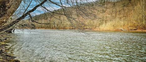 A clear river with a forested hillside in the background.