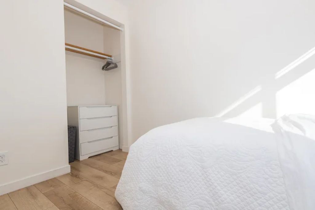 Un dormitorio con una cama blanca, un aparador blanco y un armario con barra de madera.