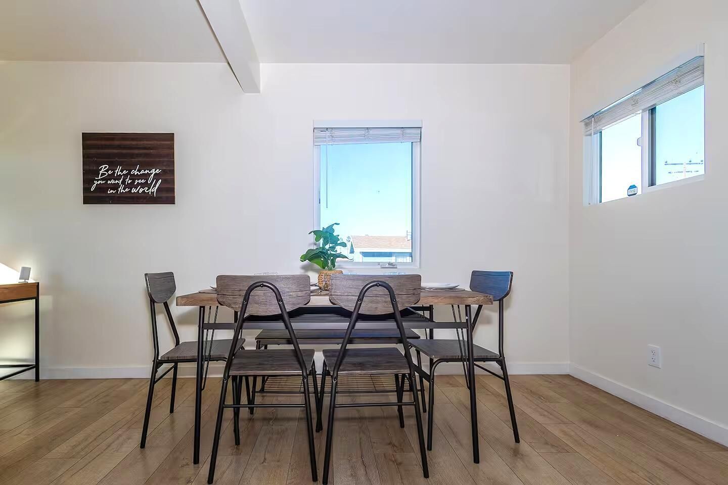 A dining area with a wooden table and metal chairs, a potted plant, and a motivational quote on the wall.