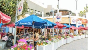 Essen im Freien mit Garnelen und Fischrestaurants, weiße Pflanzgefäße mit Blumen und einem belebten Fußweg.