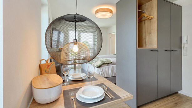 Une chambre moderne avec une table à manger pour deux personnes, un luminaire suspendu et une armoire à l’intérieur en bois.