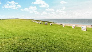 Un champ verdoyant où sont alignées, le long d’un sentier qui longe la plage, des maisons mobiles blanches.