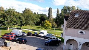 A parking area with multiple cars and a white van, surrounded by trees and a building with a tiled roof. - Magnificent F2 with terrace and parking, close to a park and 7 minutes from station (Le Mée-sur-Seine)