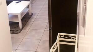 A compact living space with a sofa, a small table, a TV mounted on the wall, and a refrigerator. - Magnificent F2 with terrace and parking, close to a park and 7 minutes from station (Le Mée-sur-Seine)