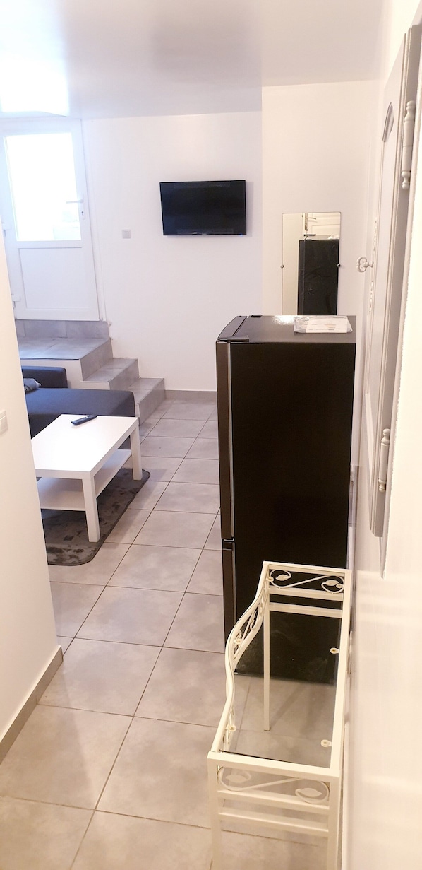 A compact living space with a sofa, a small table, a TV mounted on the wall, and a refrigerator.