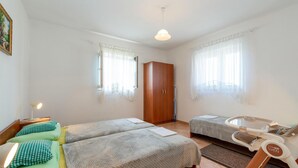 Una habitación con dos camas, un armario de madera, un baño pequeño con inodoro y una ventana con cortinas translúcidas.