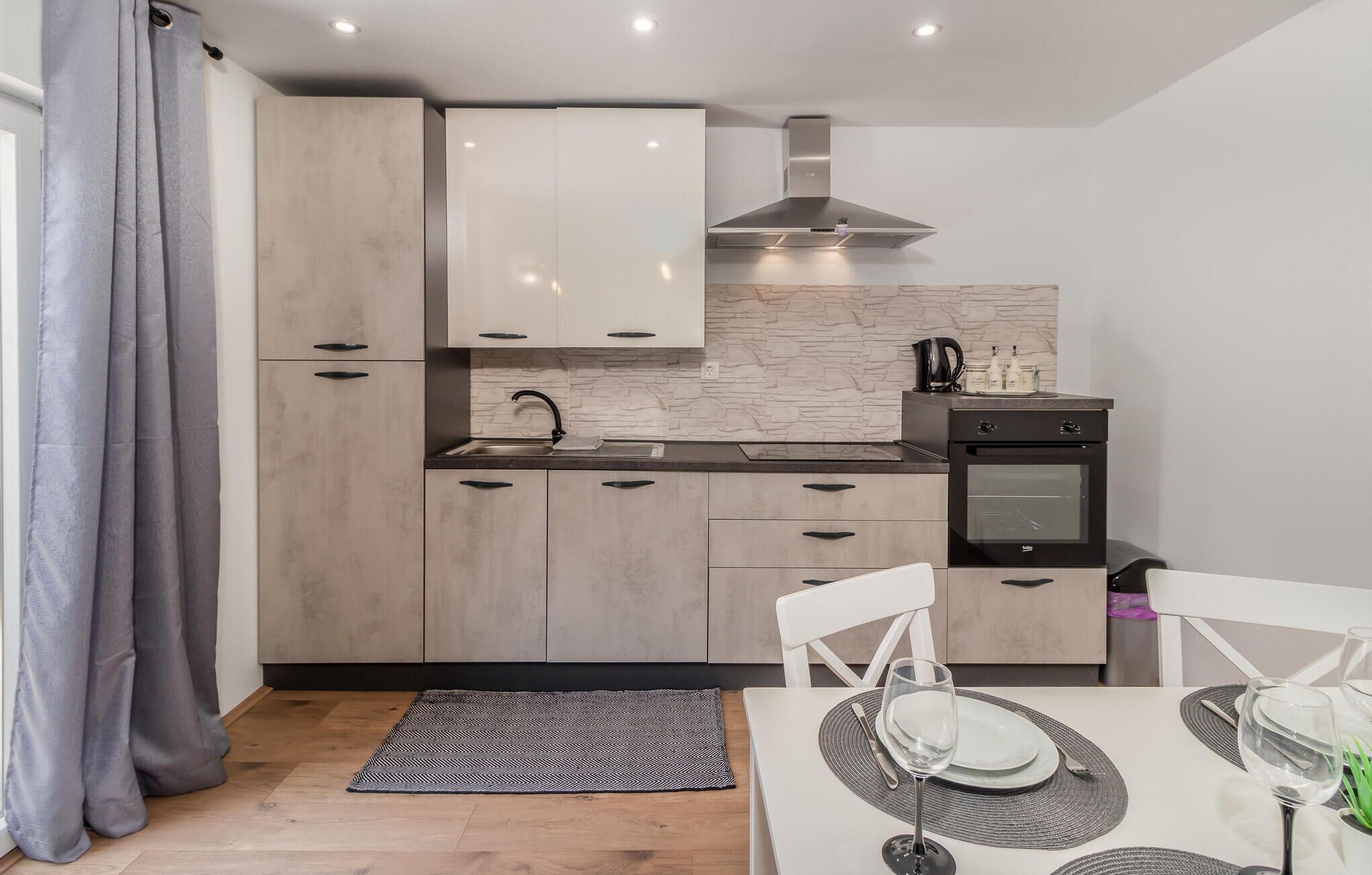 A modern kitchen with light wood cabinets, a black stove, and a stone backsplash.