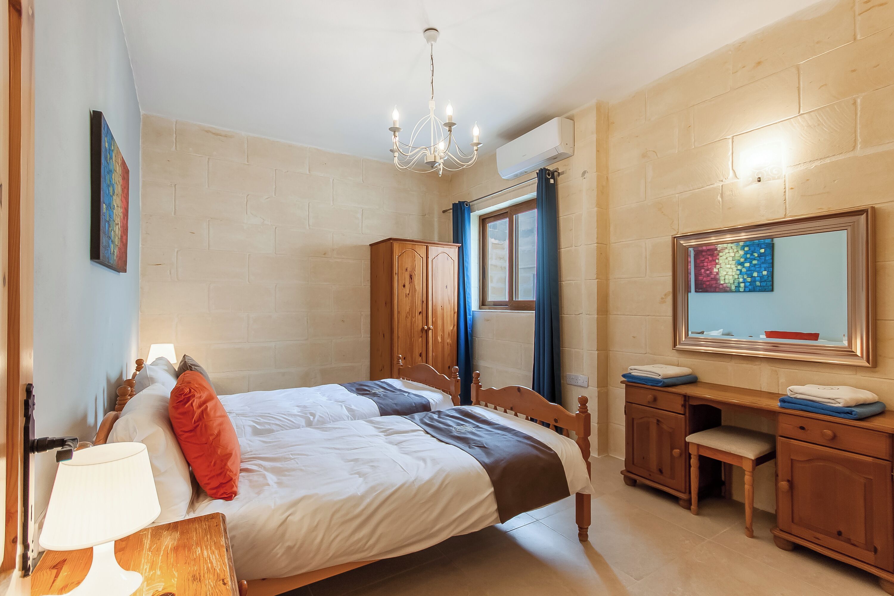 Ein Schlafzimmer mit Doppelbett, Holzschrank, Schreibtisch und großem Spiegel.