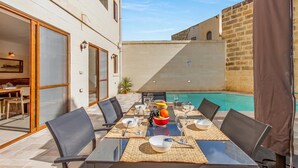 Un espace extérieur aménagé pour les repas, avec une piscine, des tables, des chaises et un panier de fruits.