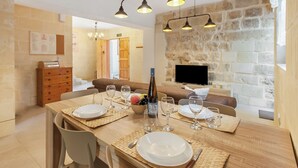 Un coin repas avec une table en bois dressée pour quatre personnes, une bouteille de vin et un mur en pierre en arrière-plan.