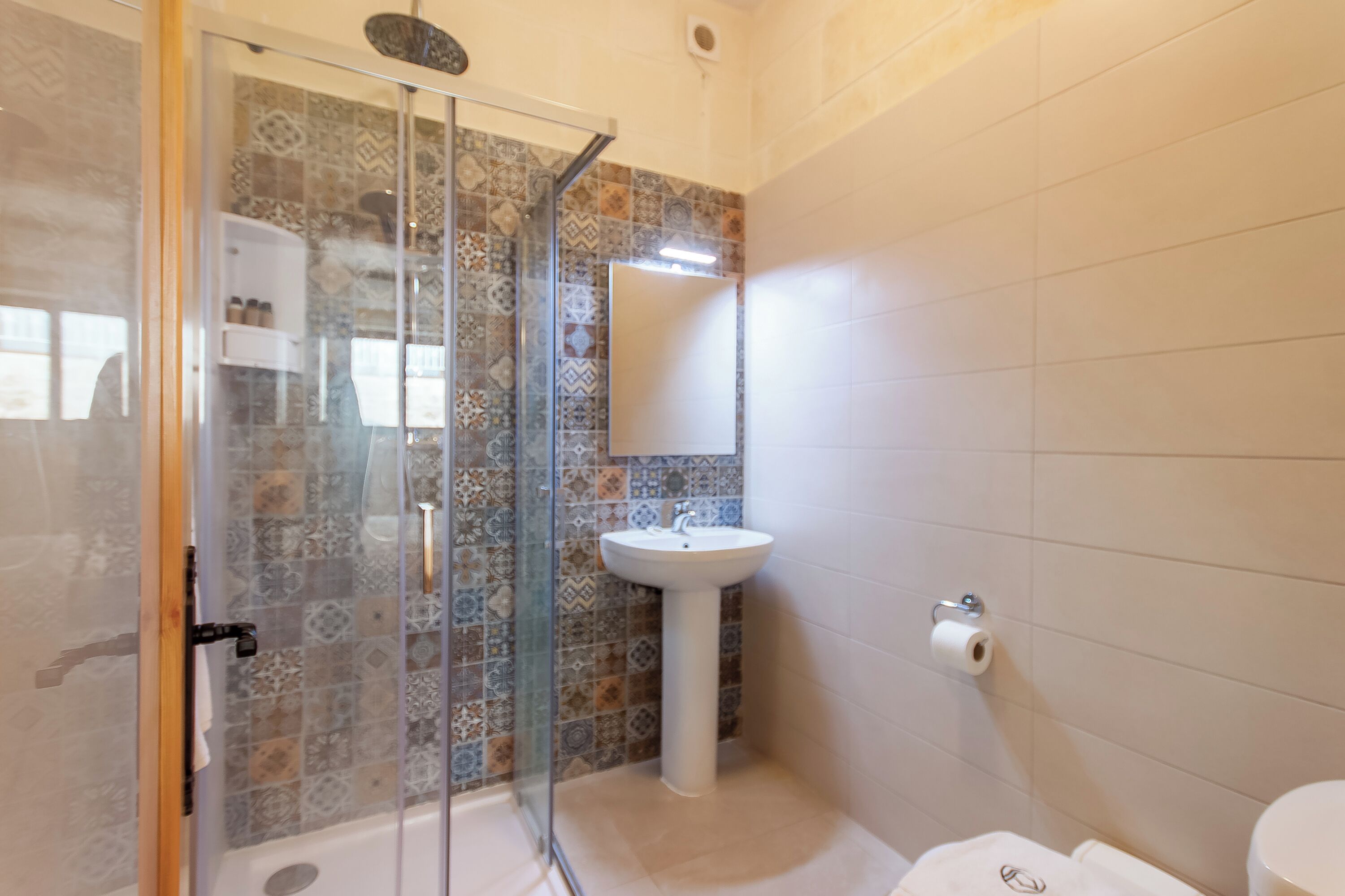 Une salle de bain avec une douche à parois de verre, un lavabo sur colonne et des toilettes.