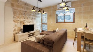 Un salon moderne avec un mur en pierre, un téléviseur à écran plat, un canapé marron, une table à manger avec des chaises et des luminaires suspendus.