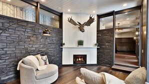 A modern living room with a stone wall, a fireplace, a mounted deer head, and a cozy seating area. - The Birch Ridge: Mission Room #2 - Queen Suite In Renovated Killington Lodge. Hot Tubs. 1 Bedroom Home (Killington)
