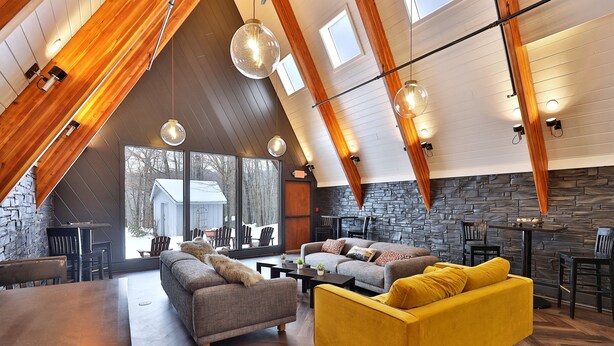 A spacious loft-style living area with high ceilings, exposed wooden beams, and large windows offering a view of the outdoors. - The Birch Ridge: Mission Room #2 - Queen Suite In Renovated Killington Lodge. Hot Tubs. 1 Bedroom Home (Killington)